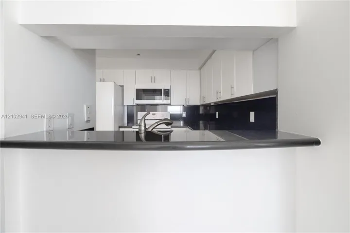 Kitchen featuring white cabinetry, contrasting dark countertops, a dark backsplash, a built-in microwave, and a stainless steel faucet