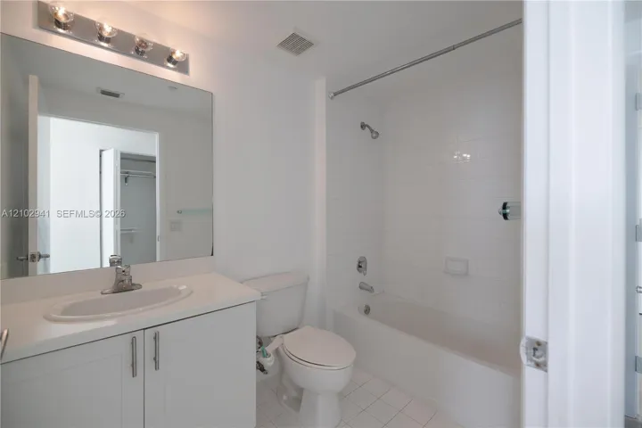 Bathroom featuring a vanity with an integrated oval sink, countertop, oversized wall mirror, four-light vanity fixture, and a tub-shower combination with white wall tile