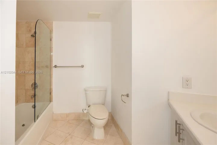 Bathroom featuring a tub-shower combination with a glass panel, stone-finish tile surround and flooring, and a solid-surface vanity countertop