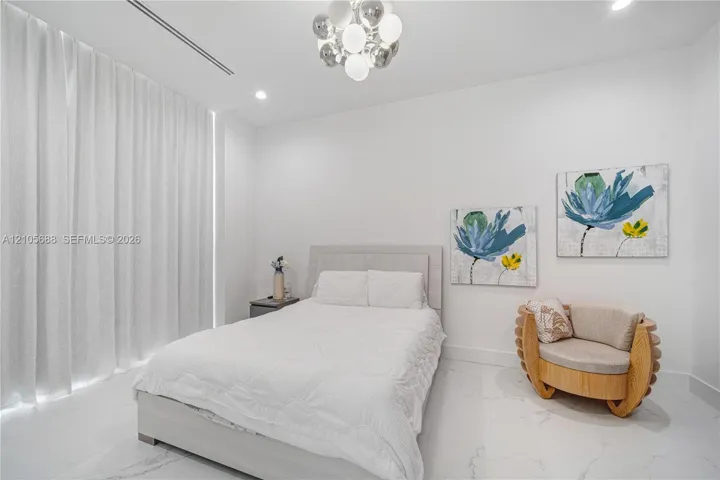 Light-filled room featuring large-format stone-finish flooring, floor-to-ceiling drapery, recessed linear lighting, and a tiered spherical chandelier