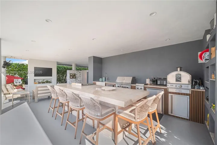 Covered outdoor kitchen featuring a stone-topped island, stainless steel grill, built-in pizza oven, and recessed ceiling lighting