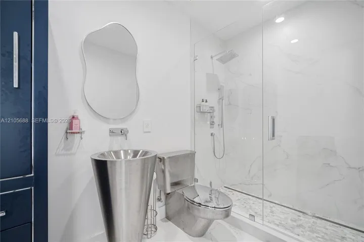 Modern bathroom featuring a metallic pedestal sink with a wall-mounted faucet, frameless glass-enclosed shower with floor-to-ceiling tile, and a contemporary mirror