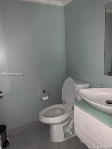 Wall-mounted vanity with a frosted glass countertop and white vessel sink, paired with a white two-piece toilet and large-format tile flooring