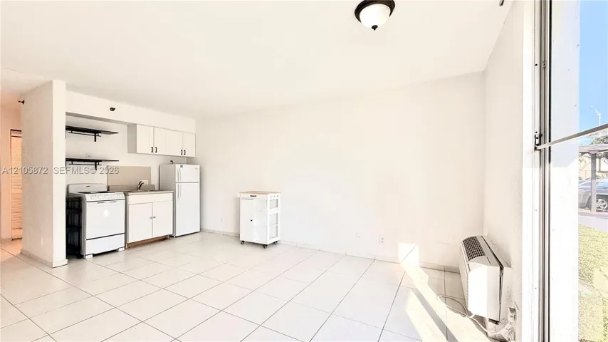 Open-concept kitchen area featuring white cabinetry, built-in shelving, white appliances, and light-toned tile flooring throughout