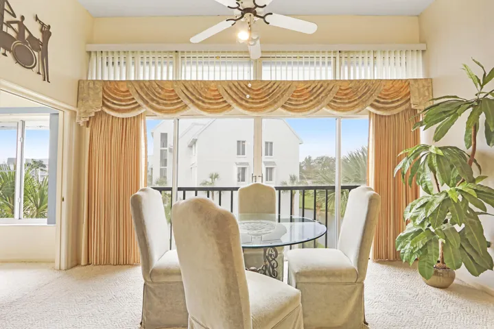 Full-height windows with vertical blinds and custom valance, recessed balcony with railing, and a ceiling fan with integrated lighting