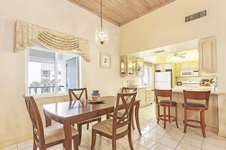 Vaulted wood-paneled ceiling with a hanging light fixture, tile flooring, and a kitchen pass-through with a breakfast bar