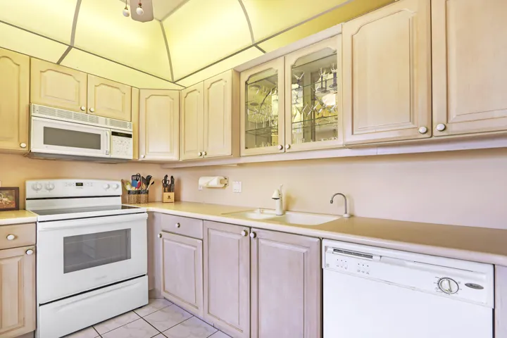 Kitchen featuring overhead cabinetry with glass-front accents, white built-in microwave, white electric range, white dishwasher, and light-toned countertops