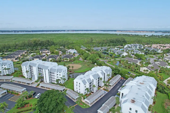 Aerial perspective of the residential community, featuring multi-story buildings, mature landscaping, paved roadways, and covered parking structures