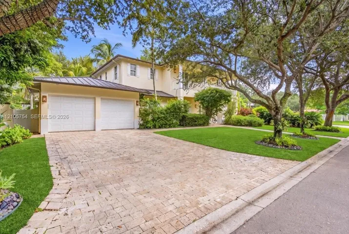 Two-story residence featuring a paved stone driveway, two-car garage, metal roof, and manicured landscaping