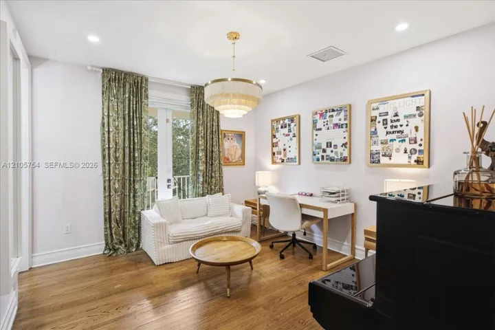 Room featuring wood-finish flooring, recessed lighting, a tiered brass chandelier, and a glass-paneled door