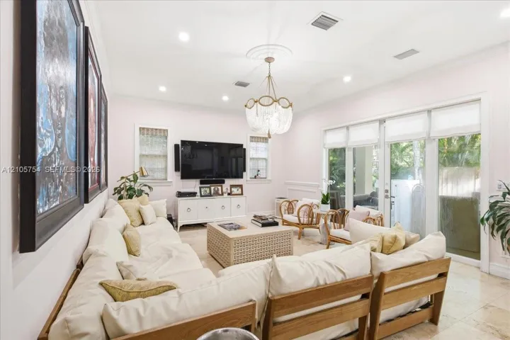 Living area featuring stone flooring, crown molding, recessed lighting, decorative ceiling medallion with a tiered chandelier, and multi-panel glass doors