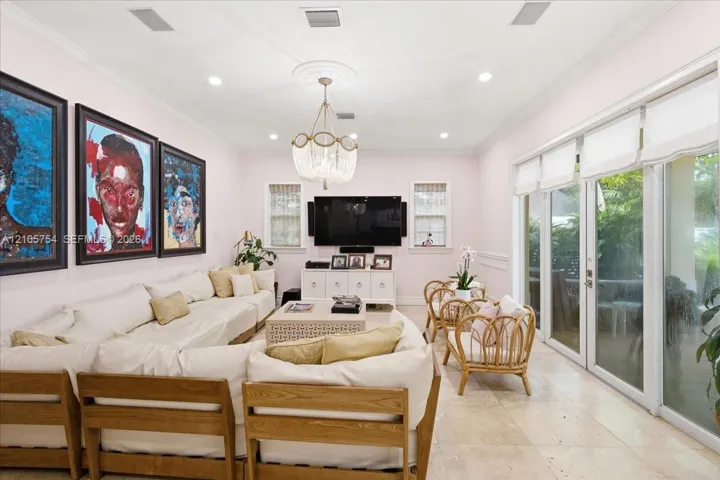 Living area featuring stone tile flooring, recessed lighting, crown molding, a decorative ceiling medallion with a tiered crystal chandelier, and floor-to-ceiling glass sliding doors