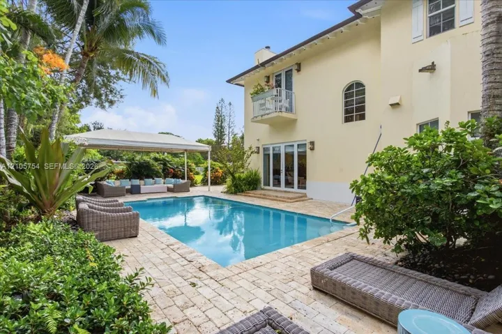 Rear exterior featuring a swimming pool, stone paver patio, covered pergola, and a second-story balcony