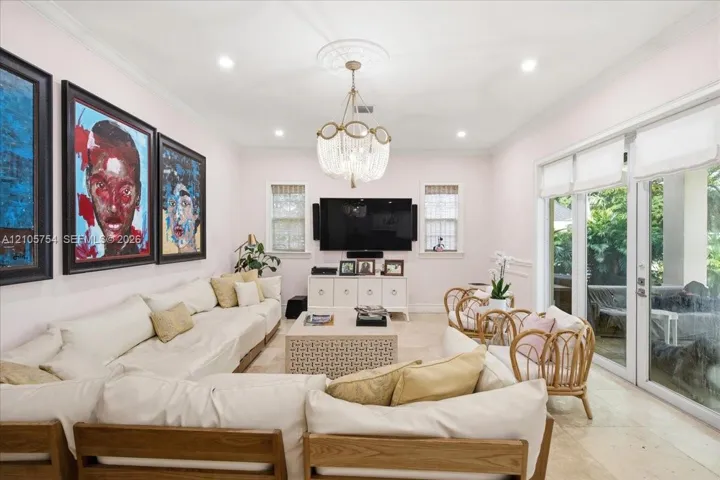 Living room featuring stone flooring, a tiered crystal chandelier with a ceiling medallion, crown molding, and glass paneled doors opening to the outdoors