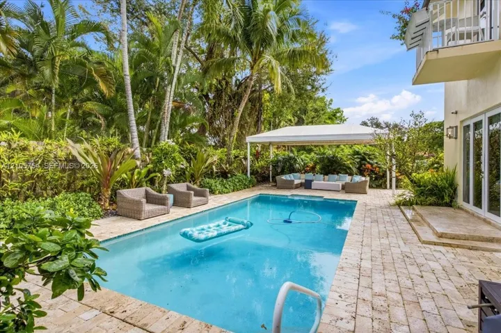 In-ground swimming pool with stone paver decking and a covered outdoor structure, bordered by established tropical landscaping
