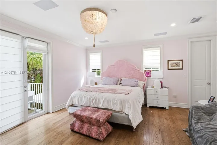 Wood-finish flooring, recessed lighting, ornate crystal-style chandelier, multi-pane windows with Roman shades, and glass-paned door opening to a balcony