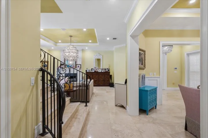 Foyer featuring tile flooring, a wrought-iron staircase railing, recessed ceiling detailing, and crystal chandelier lighting