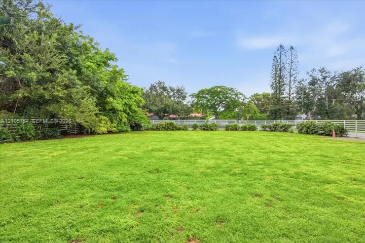 Expansive grass lawn featuring mature trees and white perimeter fencing