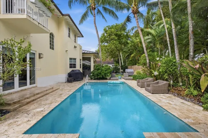 In-ground swimming pool surrounded by a natural stone deck, complemented by an exterior second-story balcony and lush tropical landscaping