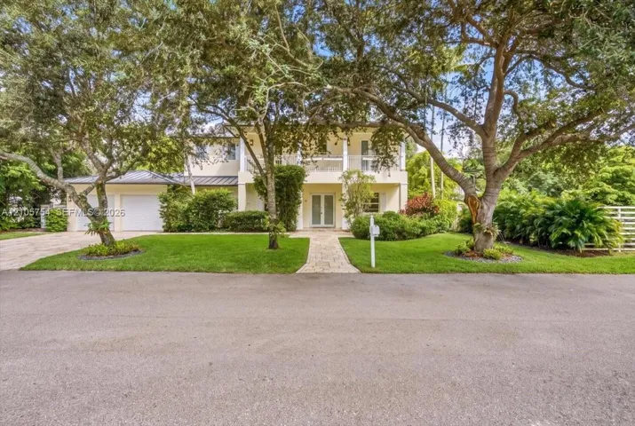 Two-story residence featuring a covered upper-level balcony, paved stone driveway, stone-finished entryway path, and a dual-car garage