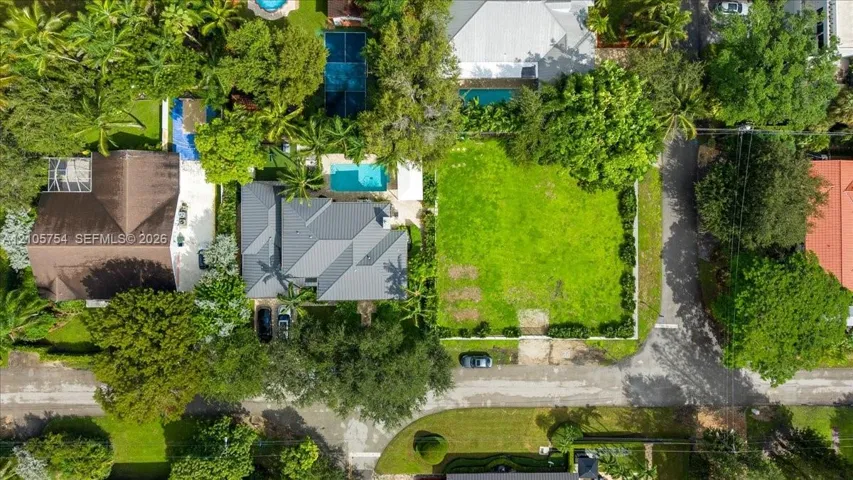 Aerial perspective of a property featuring an expansive manicured lawn, a swimming pool, and a private sports court surrounded by mature trees