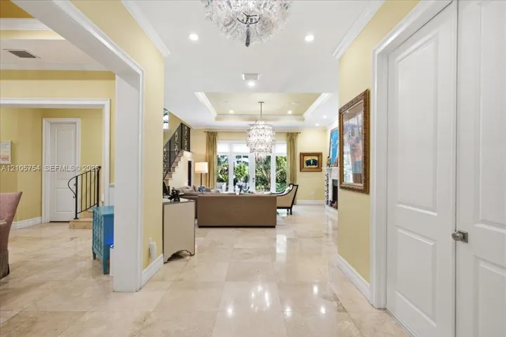 Polished stone flooring throughout, tiered tray ceilings with recessed lighting, crystal-style chandeliers, and custom crown molding
