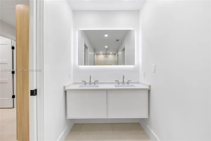 Floating double vanity with dual undermount sinks, solid-surface countertop, widespread chrome faucets, and large rectangular backlit mirror
