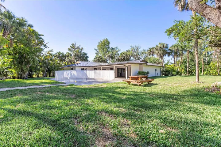 Expansive yard with mature landscaping, metal roofing, and a concrete patio area enclosed by a safety fence
