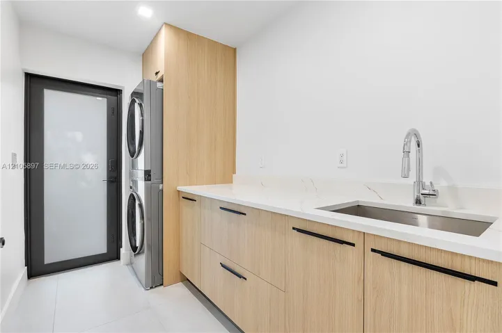 Utility space featuring custom wood-finish cabinetry, quartz countertops with integrated backsplash, a stainless steel undermount sink with a gooseneck faucet, and a matte black hardware suite