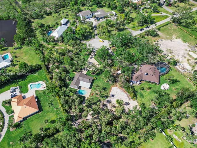 Aerial perspective of a sprawling residential property featuring mature trees, a landscaped lawn, and a private swimming pool