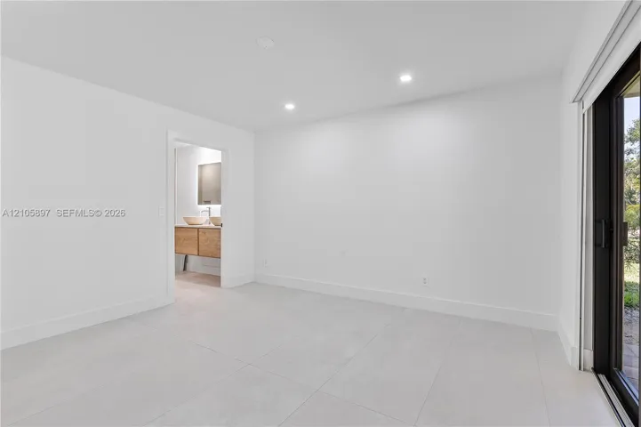 Minimalist room featuring large-format porcelain tile flooring, recessed ceiling lighting, and black-framed sliding glass doors