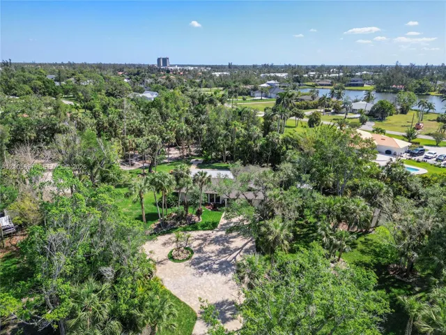 Aerial perspective featuring a sprawling lot with mature landscaping, extensive tree coverage, and a paved circular driveway