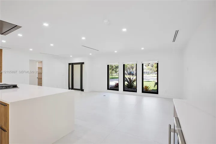 Open-concept interior featuring large-format tile flooring, recessed lighting, quartz countertops, and floor-to-ceiling windows with black framing
