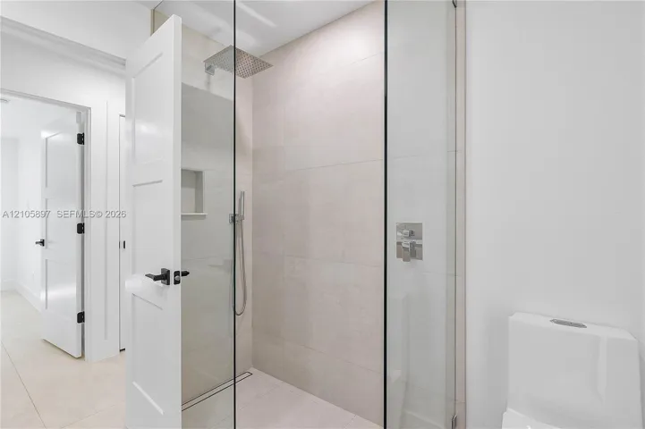 Walk-in shower featuring glass enclosure, wall-mounted rain shower head, handheld sprayer, built-in recessed niche, and large-format wall tile