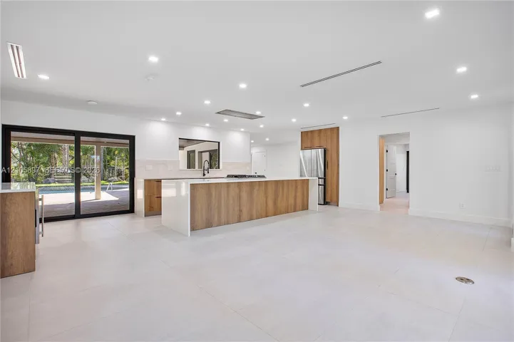 Open-concept kitchen featuring an expansive island with stone-finish countertops, wood-finish cabinetry, stainless steel refrigerator, recessed lighting, and large sliding glass doors