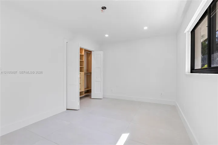 Interior room featuring neutral floor tiling, recessed lighting, and a closet with custom built-in shelving