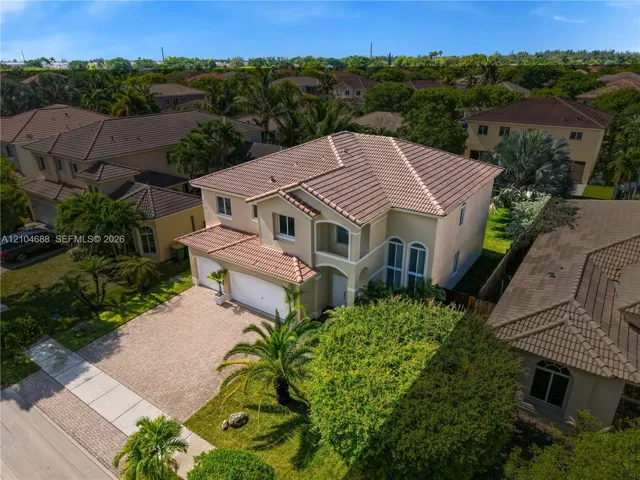 Two-story residence featuring a terracotta-tiled roof, stucco exterior, multi-car garage, arched window accents, and a paved driveway