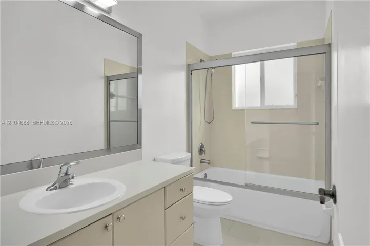 Bathroom featuring a solid-surface countertop with an integrated basin, large-format mirror with a metallic frame, vanity cabinet storage, and a bathtub with a sliding glass enclosure