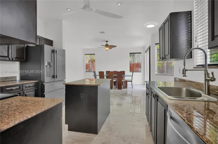 Kitchen featuring dark-finish cabinetry, stone countertops, stainless steel appliances, a center island, and tile flooring