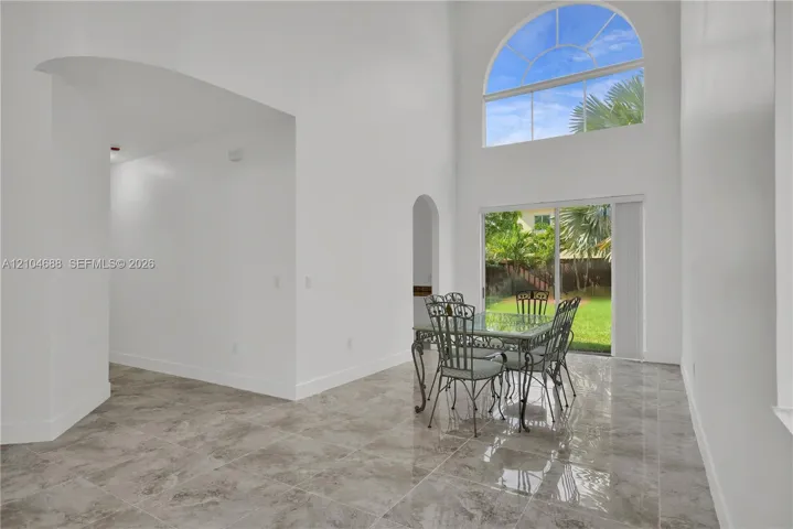 High-ceiling room featuring large-format tile flooring, arched wall openings, and a prominent floor-to-ceiling arched window with sliding glass door access to the exterior