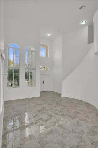 High-ceilinged entry featuring stone-finish tile flooring, arched windows, recessed lighting, and a curved architectural wall