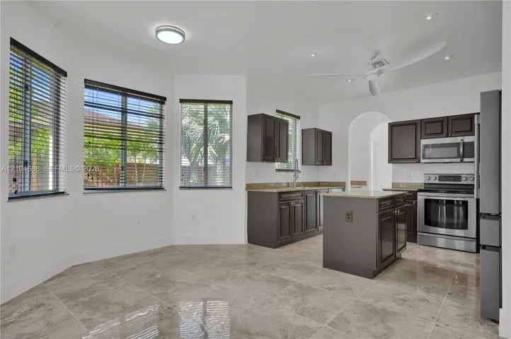 Kitchen featuring dark-toned cabinetry, stone countertops, a central island, stainless steel appliances, and tile flooring