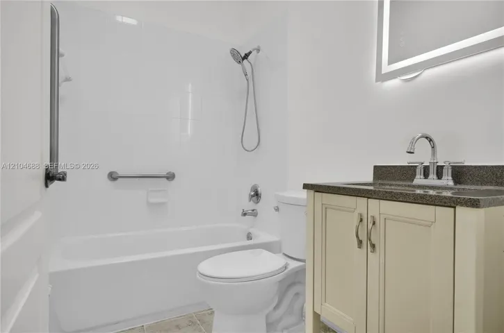Bathroom featuring a vanity with neutral-toned cabinetry, a stone-composite countertop, an integrated sink, an illuminated vanity mirror, and a tiled tub surround with a handheld shower fixture