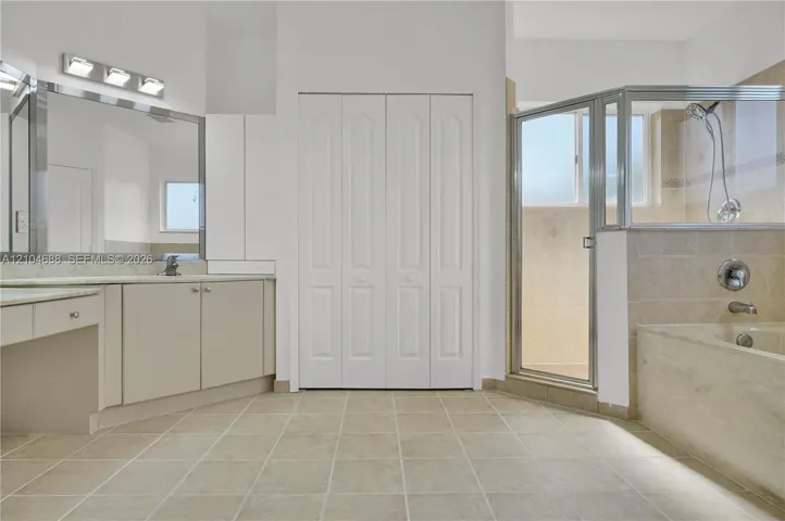 Bathroom featuring a vanity with a large mirror, a tiled soaking tub, a glass-enclosed shower, tile flooring, and floor-to-ceiling bi-fold closet doors