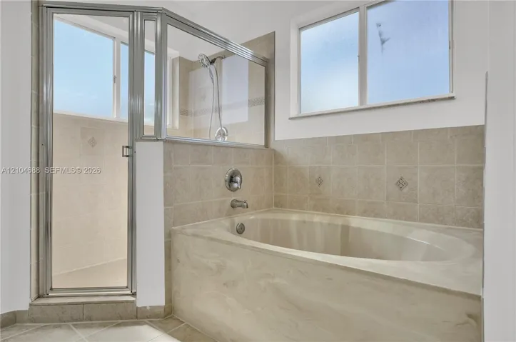 Soaking tub with a solid-surface surround, tiled shower enclosure, metal-framed glass shower door, and privacy-glass windows
