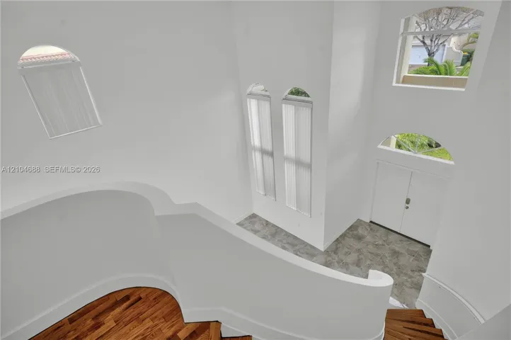Foyer featuring a double-door entrance, stone-finish flooring, curved staircase with wood-finish treads, and multi-level arched windows