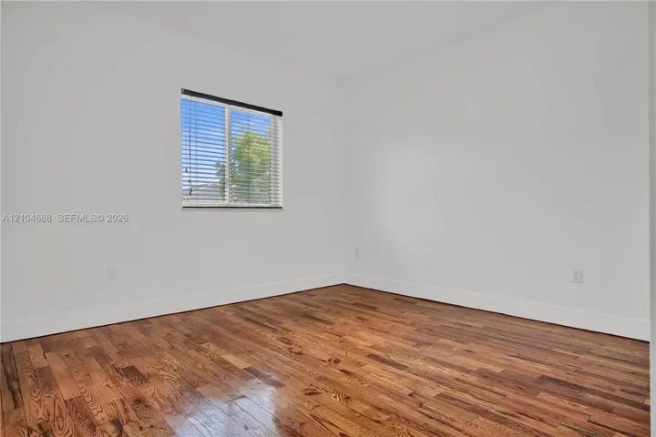 Interior space featuring wood-finish flooring, white walls, and a window with installed horizontal blinds