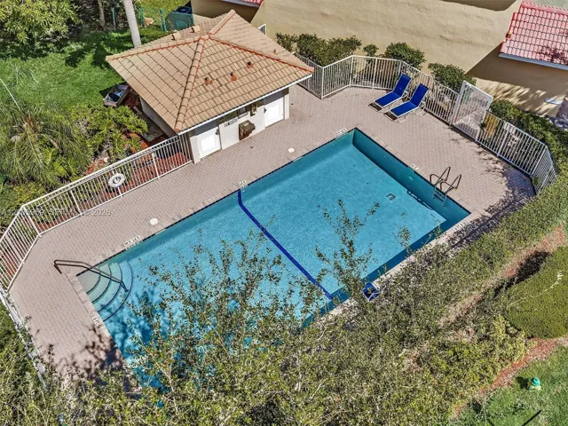 Rectangular swimming pool featuring a tiled deck, built-in structural gazebo with a tile roof, metal perimeter fencing, and stainless steel ladder access
