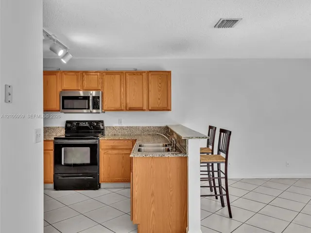 Kitchen featuring wood cabinetry, stone-finish countertops, stainless steel microwave, black electric range, and tile flooring