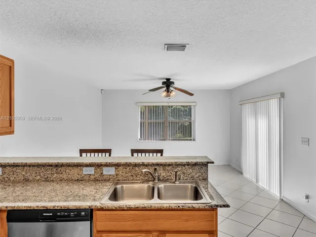 Kitchen featuring a stone-surfaced breakfast bar, double-basin stainless steel sink, wood-finish cabinetry, tile flooring, and sliding glass patio doors